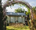 Evening wedding ceremony in garden, arch with white branches, brown wooden chairs